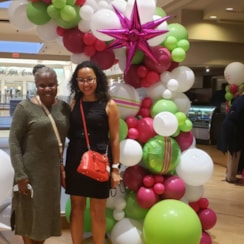 Two women standing in front of colorful balloon arch at event