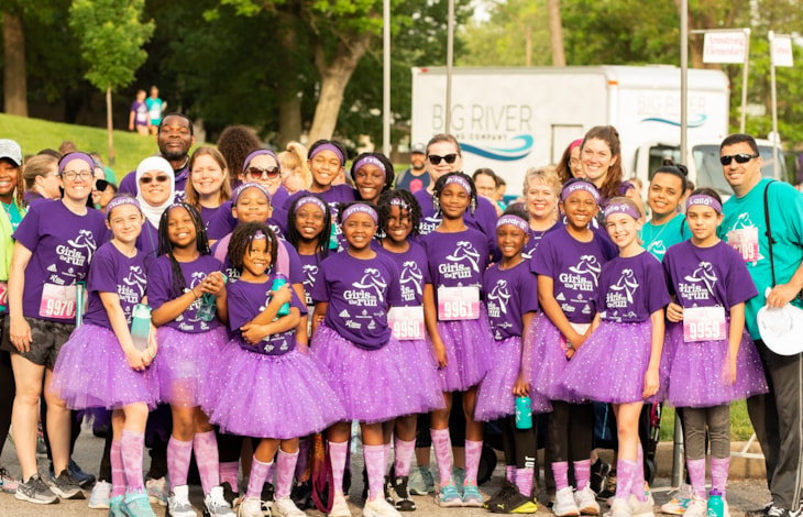 Group of GOTR participants in purple shirts and purple tutus smiling together before the race